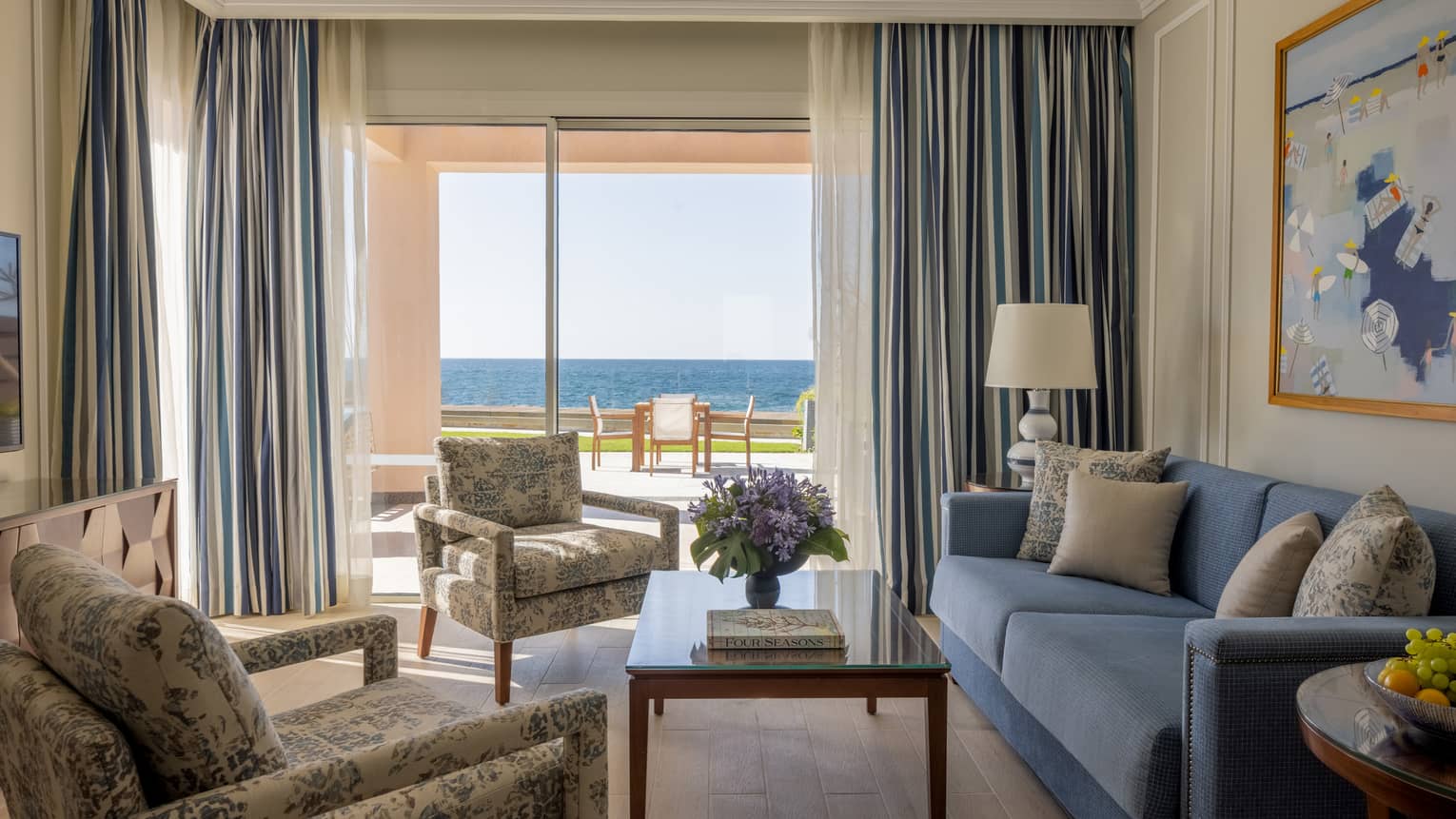 One-Bedroom Beach villa living area with twin patterned armchairs, blue sofa, sliding glass door to terrace
