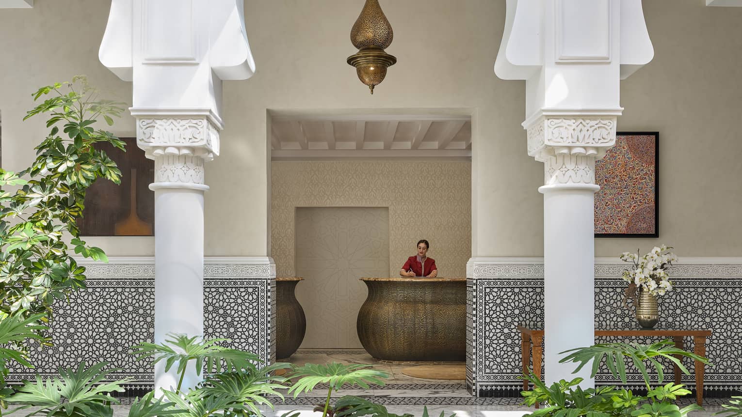 Woman at reception desk at Moroccan hotel with atrium and greenery