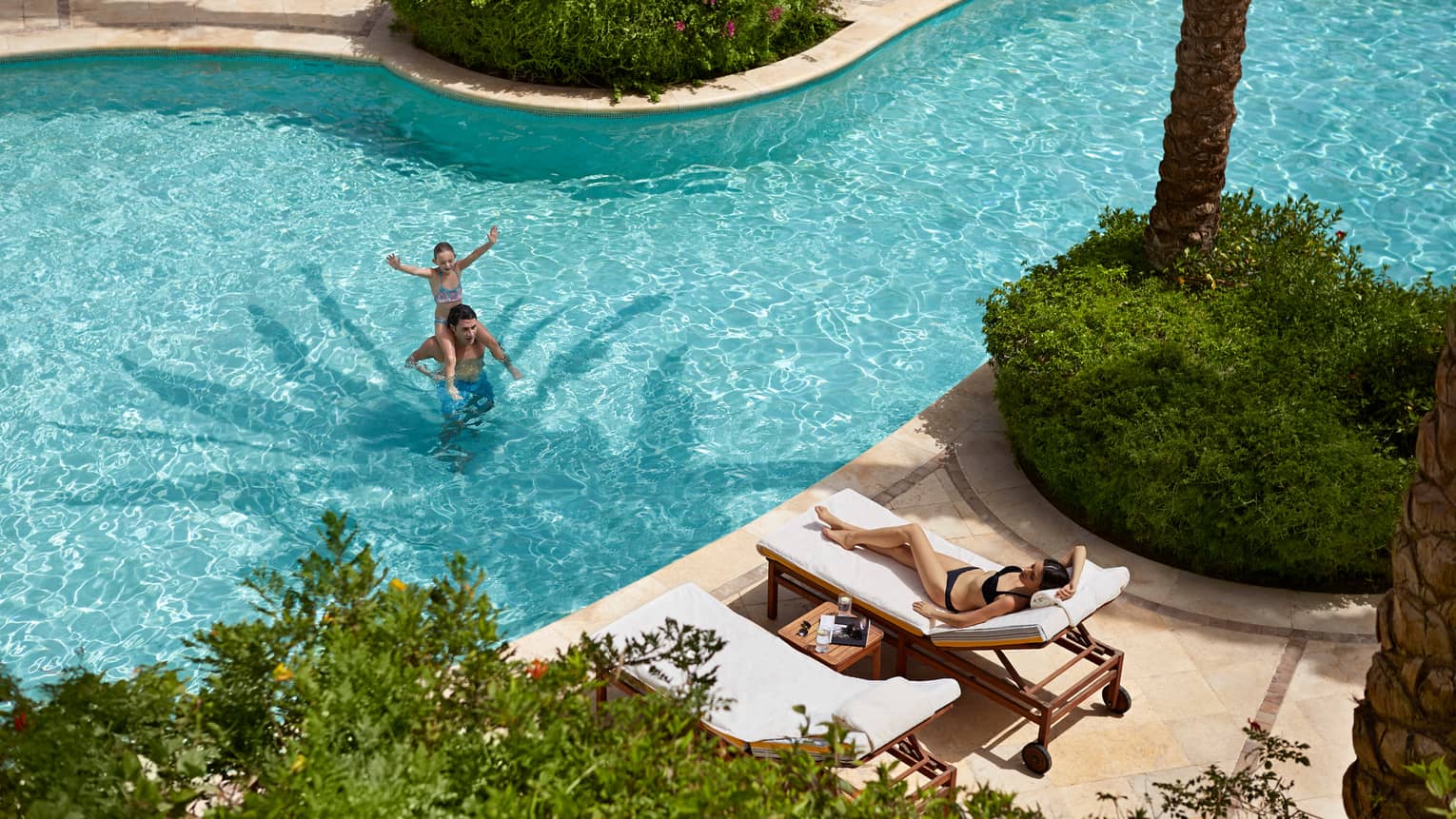 Aerial view of Gezira Pool, young girl on dad's shoulders in water, woman in bikini sunbathes on chair,Aerial view of pool, young girl on dad's shoulders in water, woman in bikini sunbathes on chair