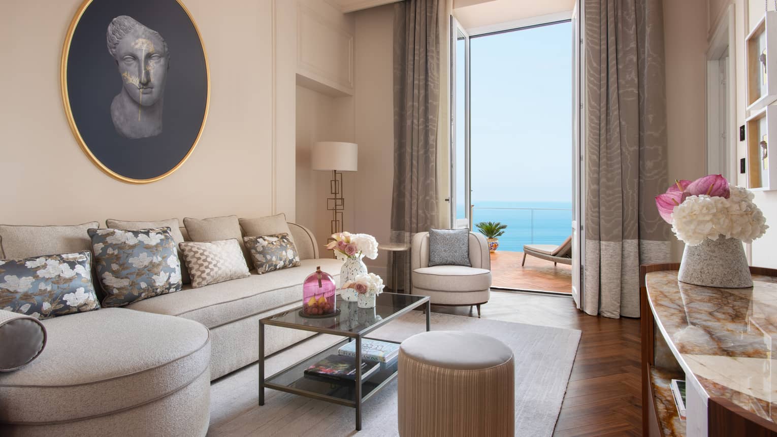 Living room with curved, taupe-coloured sofa, doors leading to ocean-view balcony