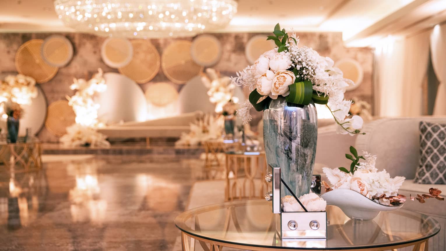 Elegant ballroom with dome chandelier, white roses in silver vase on glass coffee table