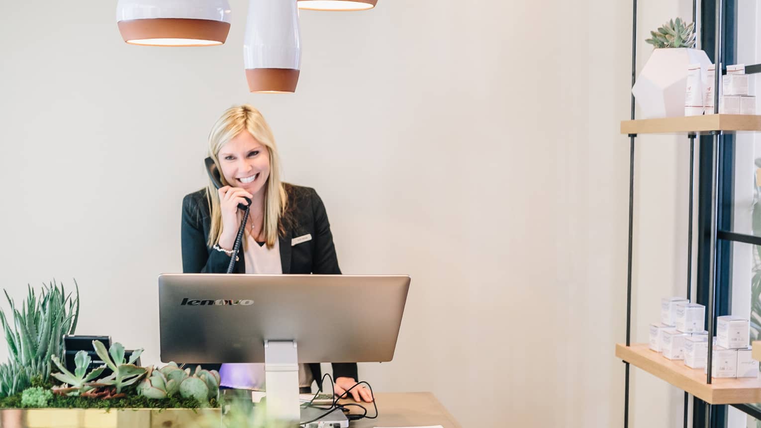 Smiling spa staff on telephone behind large silver computer screen