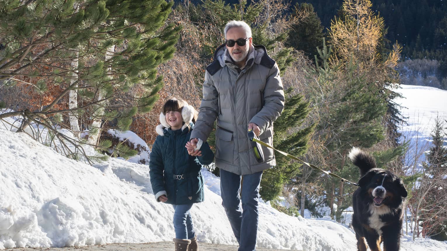 Man holding boy’s hand while walking with a dog on snowy trail