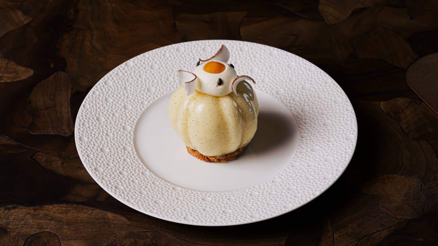 Delicate dessert served on a white round plate on a dark brown table