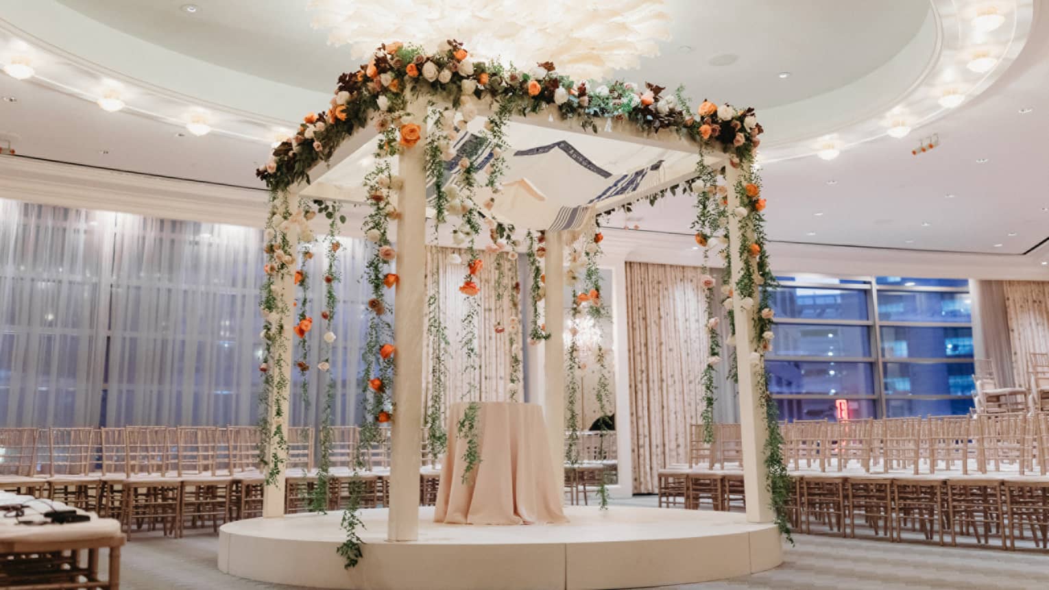 An alter made of white wood with bright flowers covering it, in a room with rows of seats.