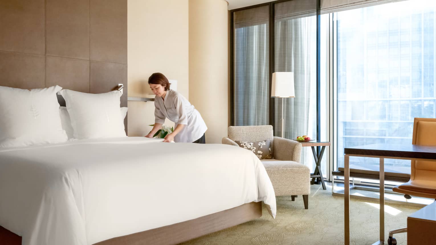 Hotel staff making a Four Seasons bed with white linens in a hotel room