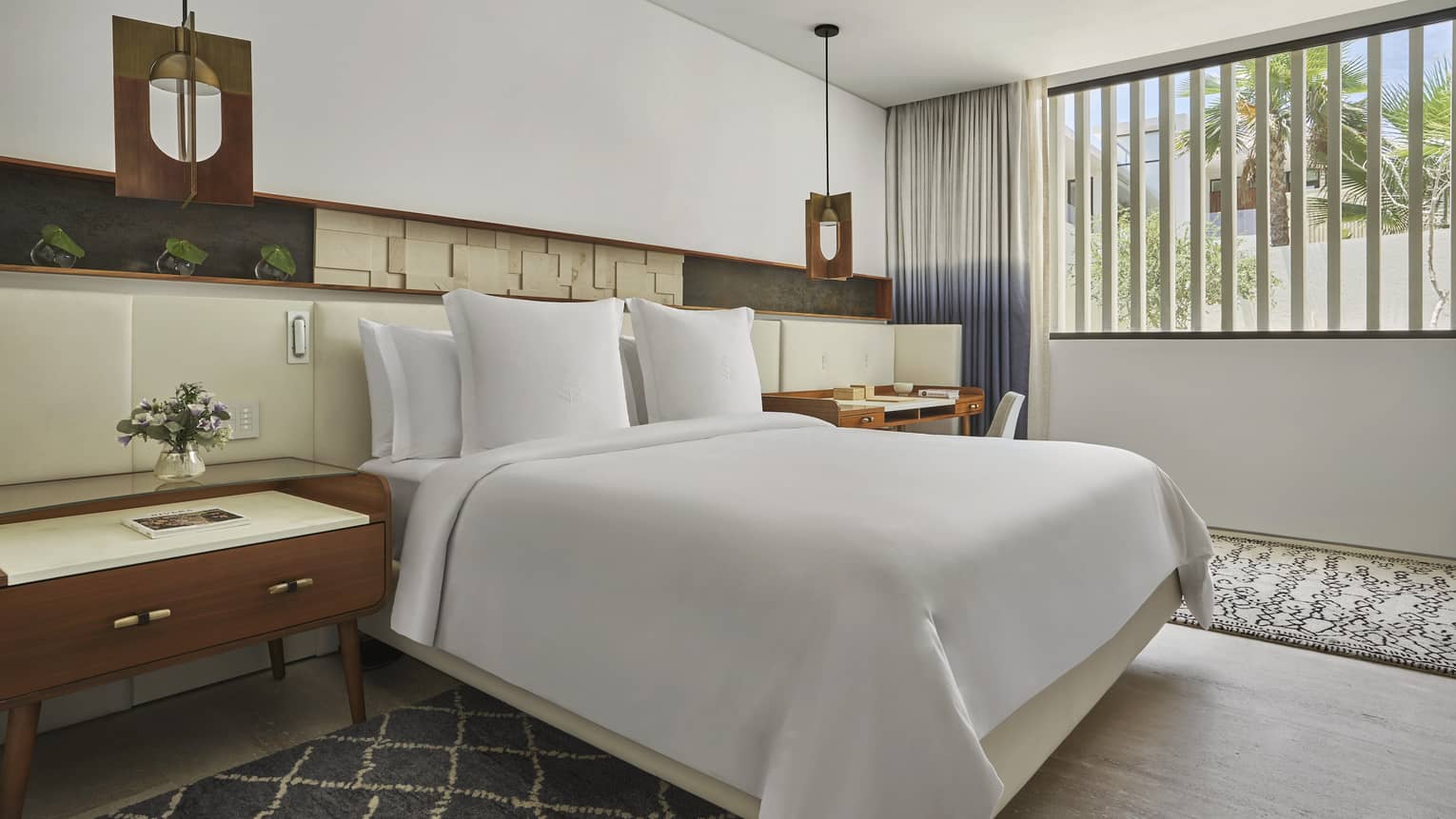 Two Bedroom Ocean View Suite with King bed, white linens, grey and white accent rugs, full-length headboard, cherry oak side table, window with two-tone curtains