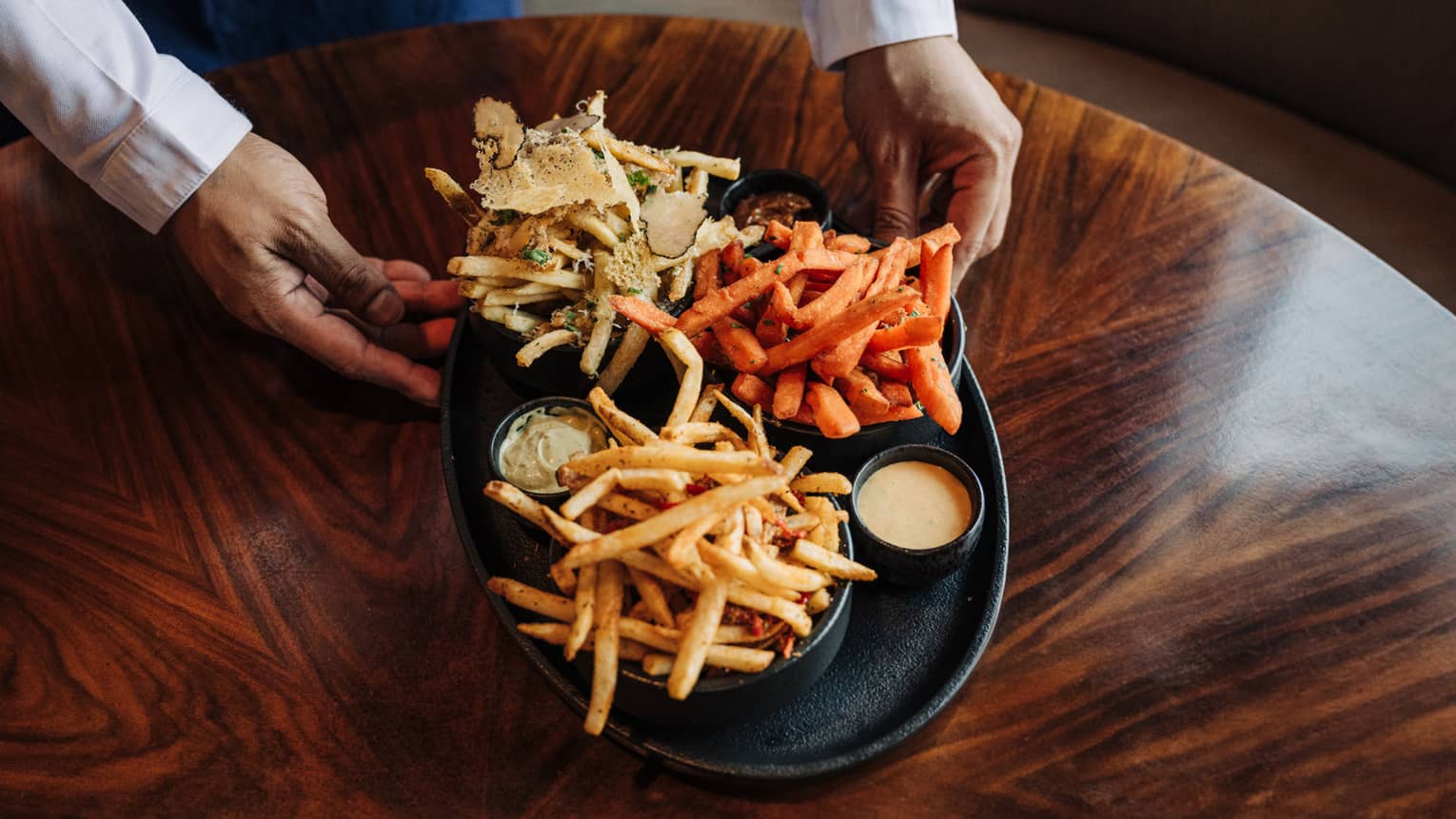 Black platter featuring a trio of three different kinds of French fries along with three dipping sauces
