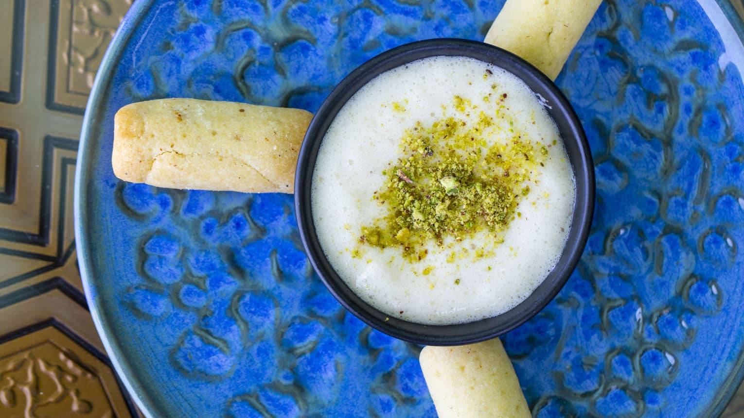 An overhead view of a white sauce with spices sprinkled on top and bread sticks around it, on a blue pottery dish