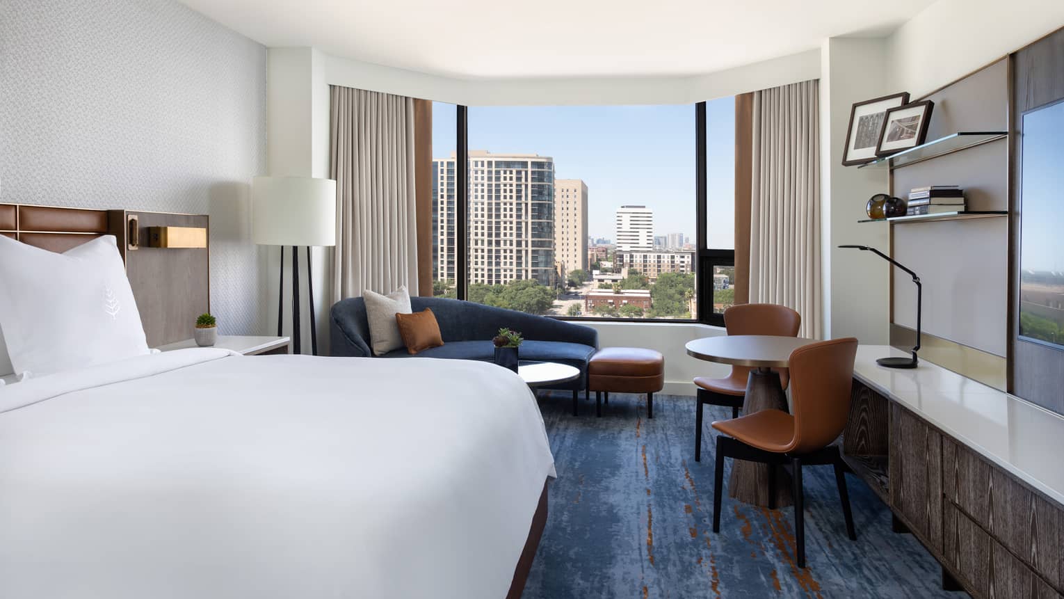 Hotel room with king bed, dark blue chaise lounge, table and two leather chairs, blue carpeting