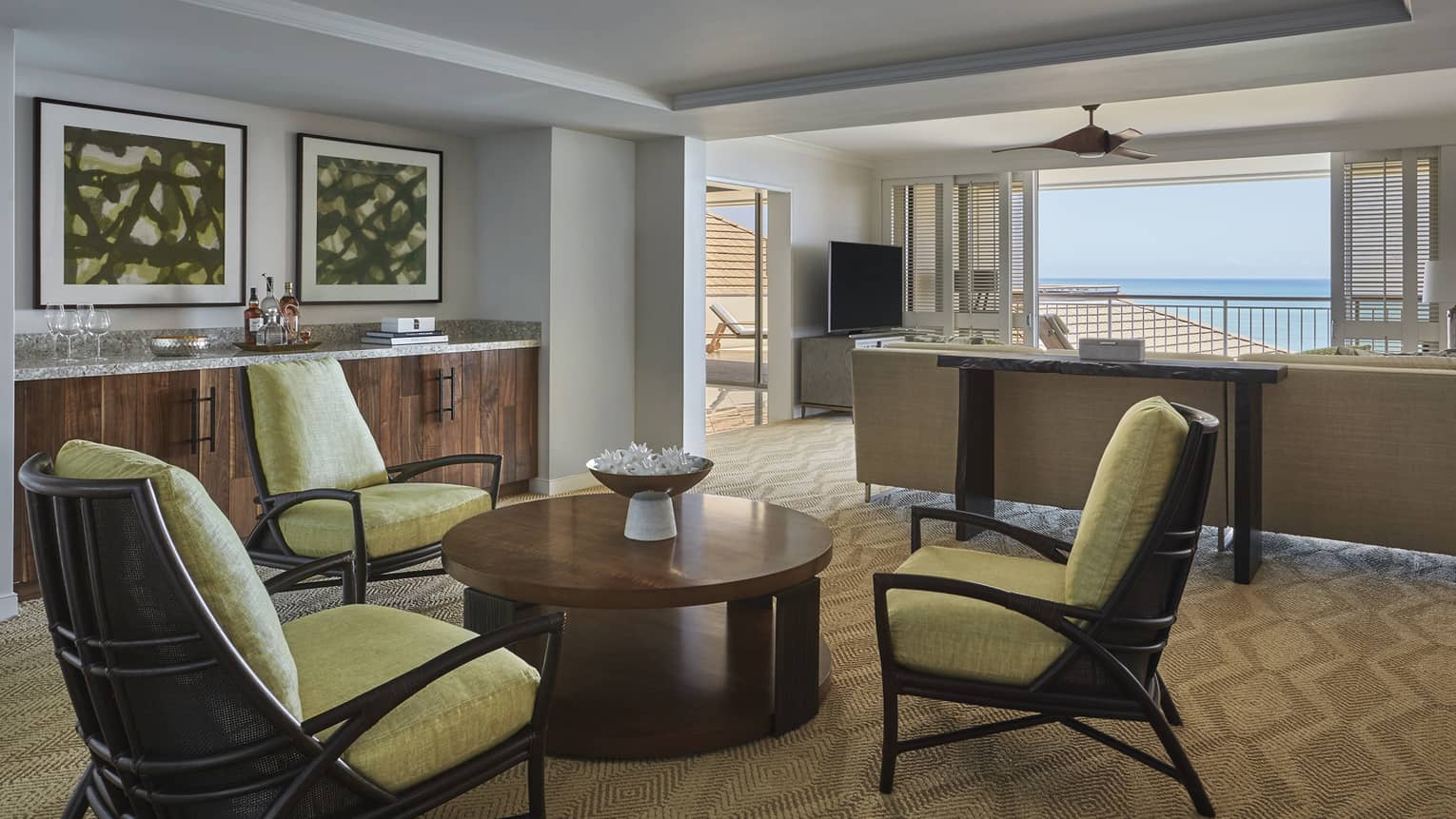 Sitting area with three wooden arm chairs with light green cushions, circular coffee table