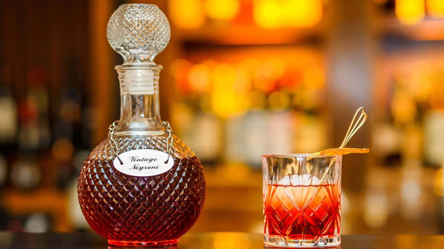 Vintage Negroni liquor in crystal bottle beside cocktail in rock glass
