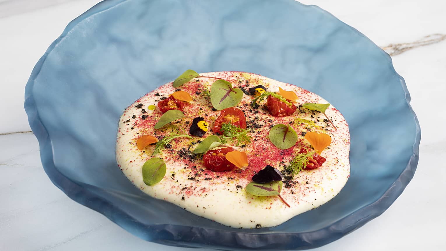 Potato foam topped with octopus, tomatoes and various greenery served in a blue platter.