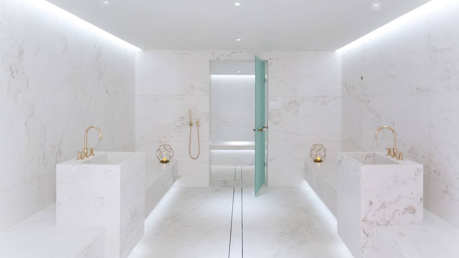 Minimalist spa room with white marble walls, brass fixtures, a glass door and soft ambient lighting