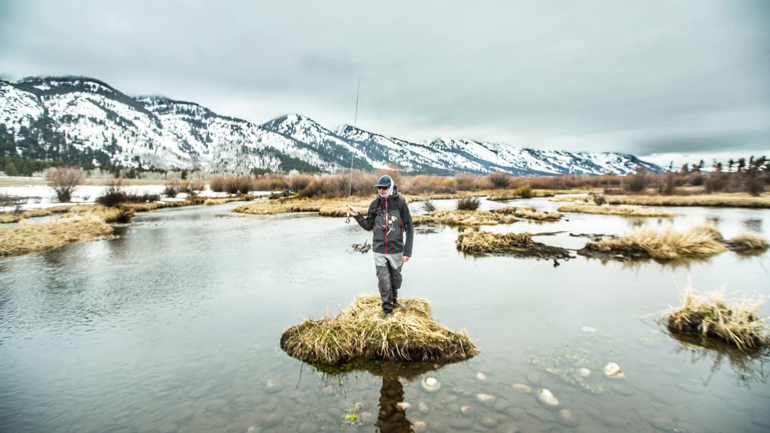 A man standing on a small piece of land surrounded by water holding a fishing rod.