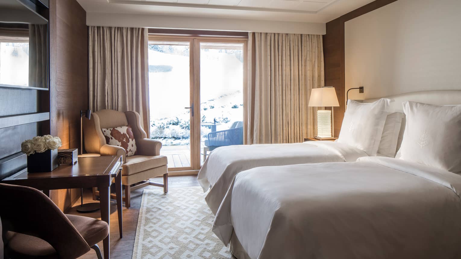 Deluxe Room double beds facing TV, table, armchair, by glass balcony doors