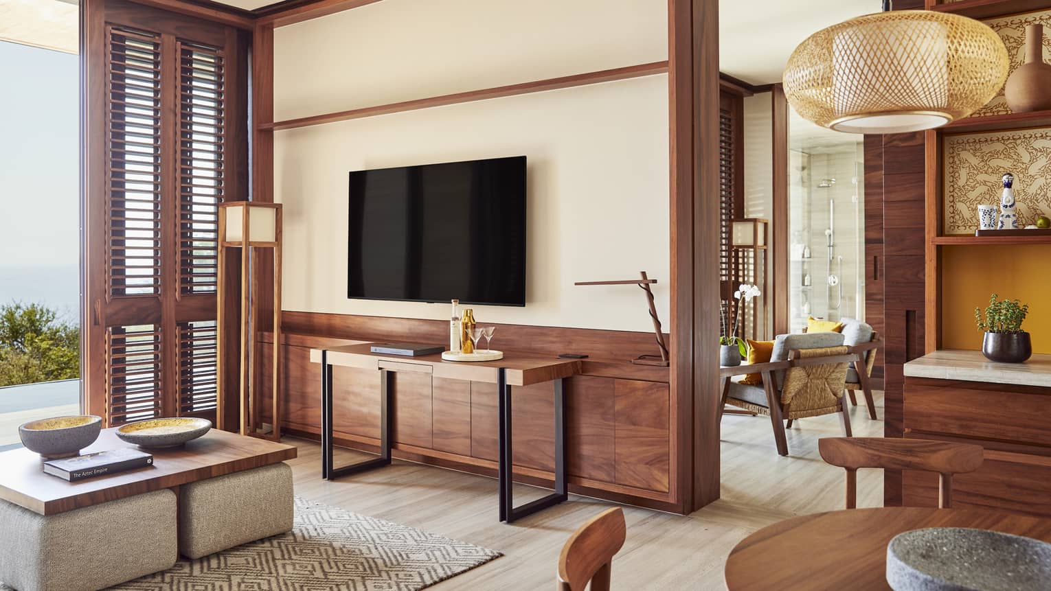 Modern living area with wooden accents, a wall-mounted TV and a cozy seating space. The room features a blend of contemporary furniture, natural light and a view of the ocean.