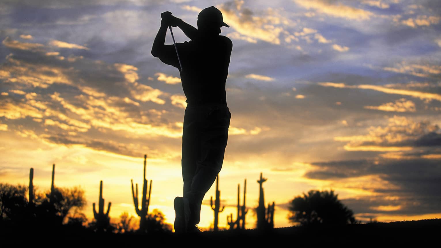 Silhouette of golfer swinging club against sunset sky at Troon North golf course