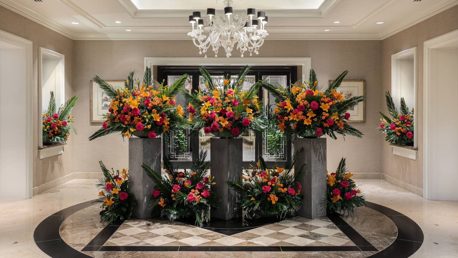 Elegant, artistic red, orange and green floral arrangements adorn a bright, spacious and neutral-toned lobby area.