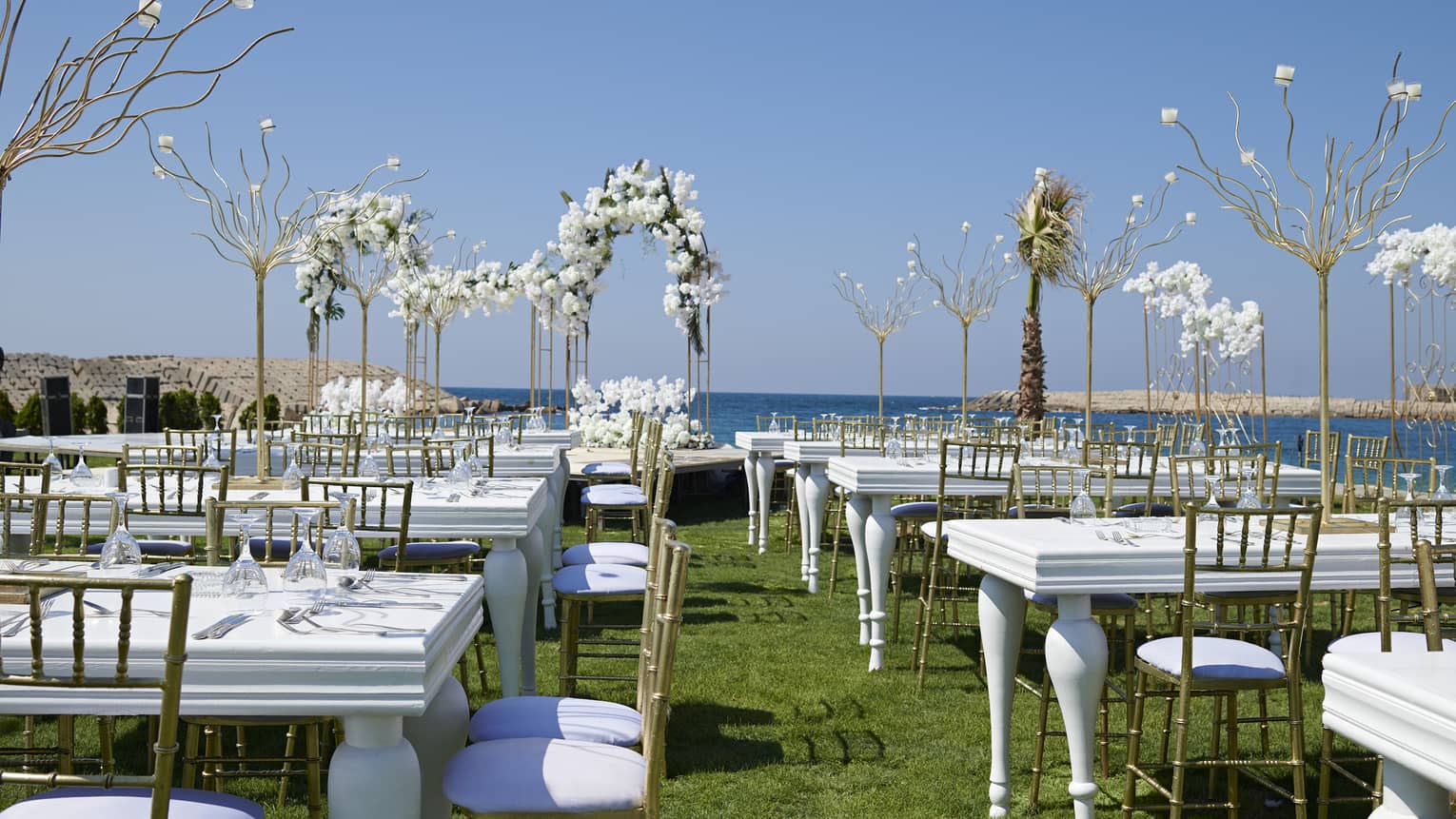Oceanfront lawn set for a wedding with white tables, gold chairs and white orchids