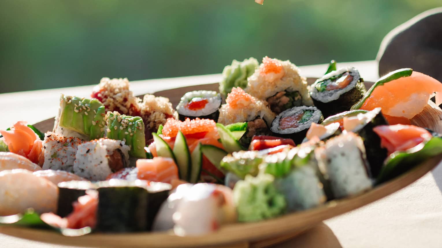 Hand pinching chopsticks, holding a piece of sushi over a plate of assorted sushi