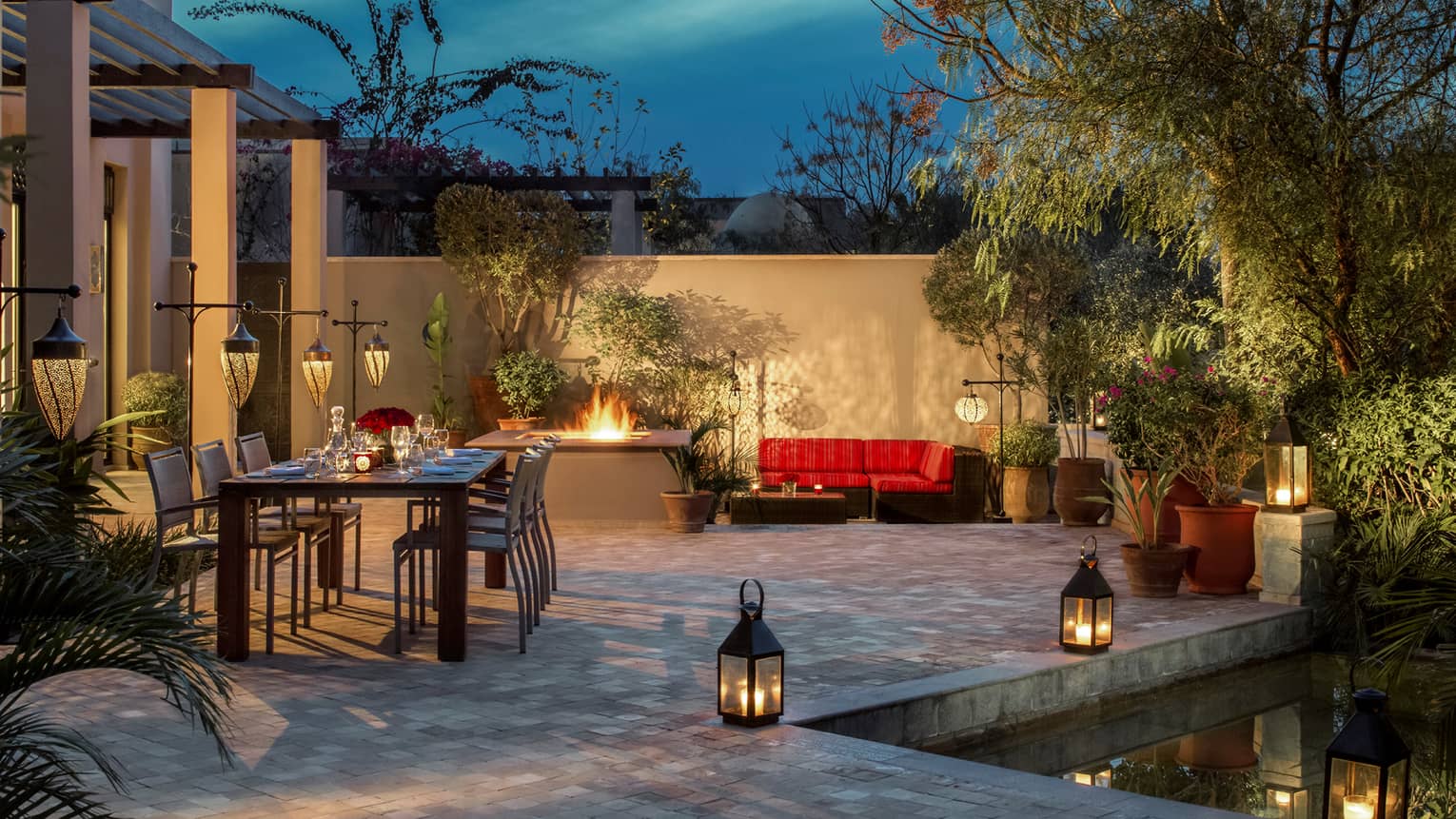 Two-bedroom villa patio with long candle-lit private dining table, outdoor fireplace, lanterns along pool