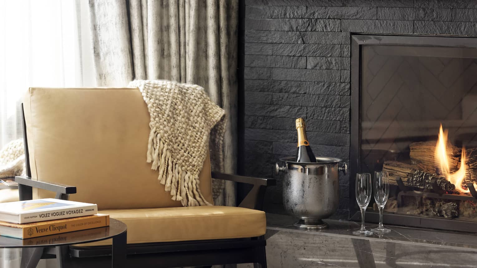Leather chair, round side table, fireplace, ice bucket with bottle of champagne and two flutes