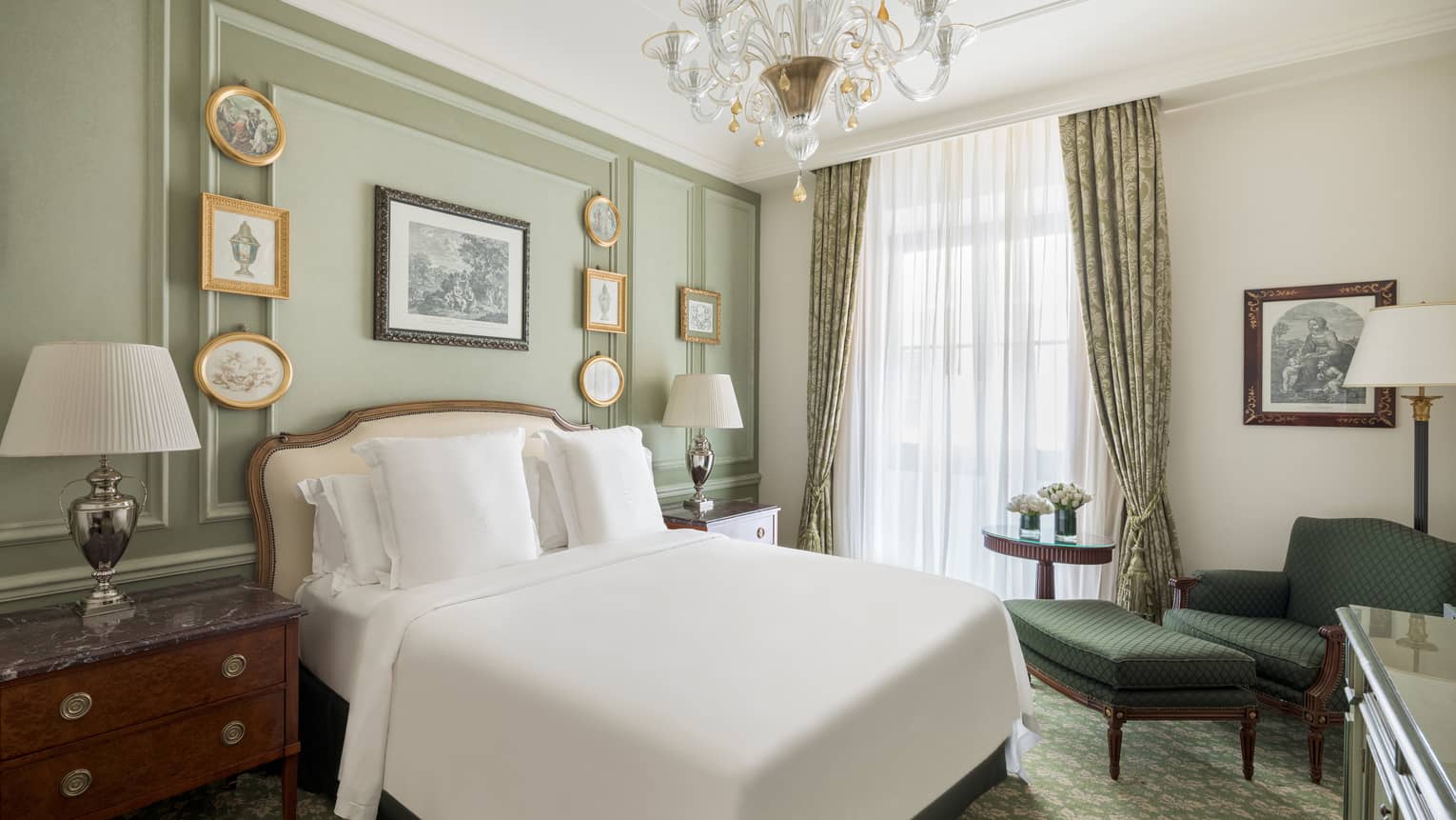 Bedroom with light green walls, small picture frames, crystal chandelier, white king bed