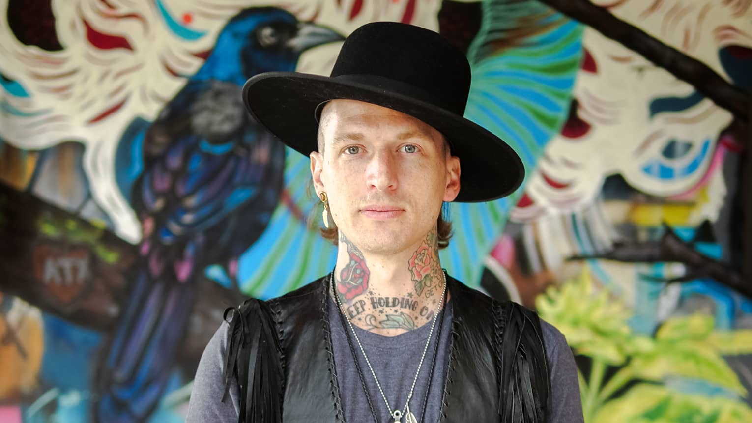 A portrait of Muralist Jason Eatherly in front of his mural on the patio at Ciclo.