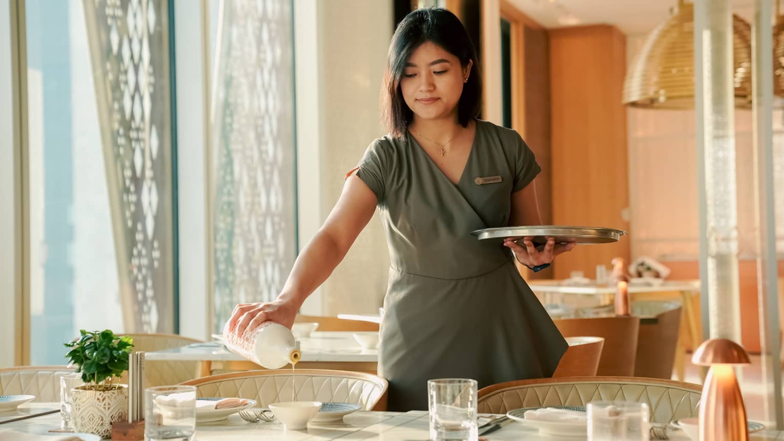 Server stand over a table in a restaurant pouring dipping oil into a small white bowl