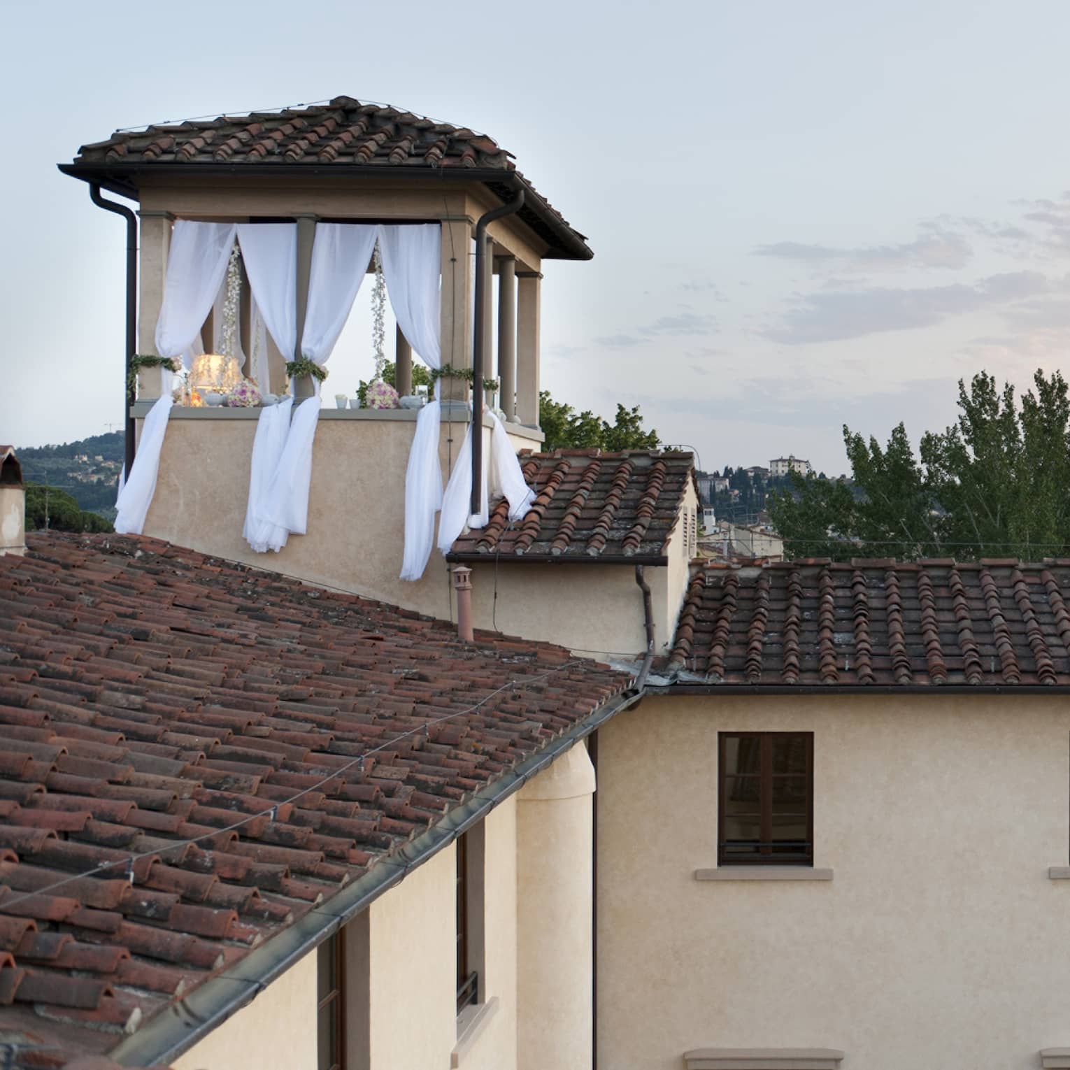 Looking across the red tiled rooftop of the Hotel to a small terrace with white flowing curtains and romantic decorations.