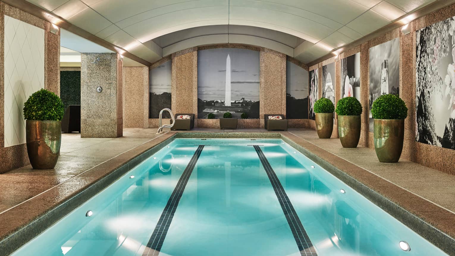 Long indoor lap swimming pool, large gold planters on deck, wall with black-and-white mural of the Washington Monument