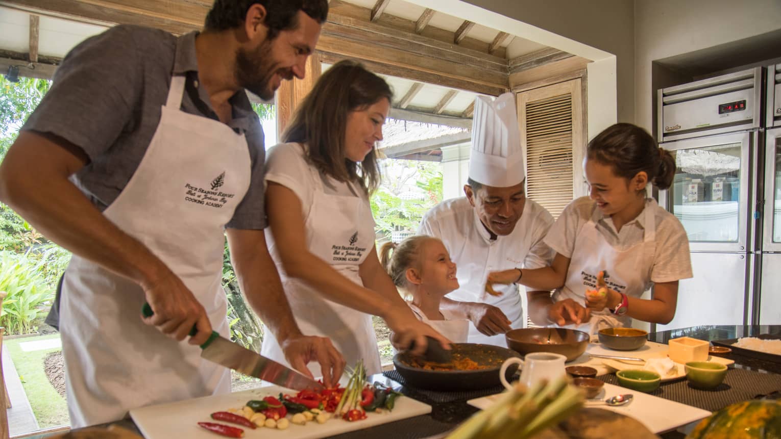 A smiling chef oversees a family joyfully indulging in a private cooking class at Four Seasons