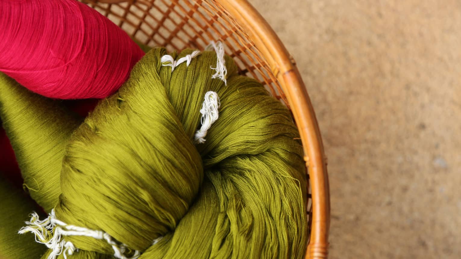 Extreme close-up of bundles of shiny, silky fuchsia- and chartreuse-coloured yarn in a wicker basket.