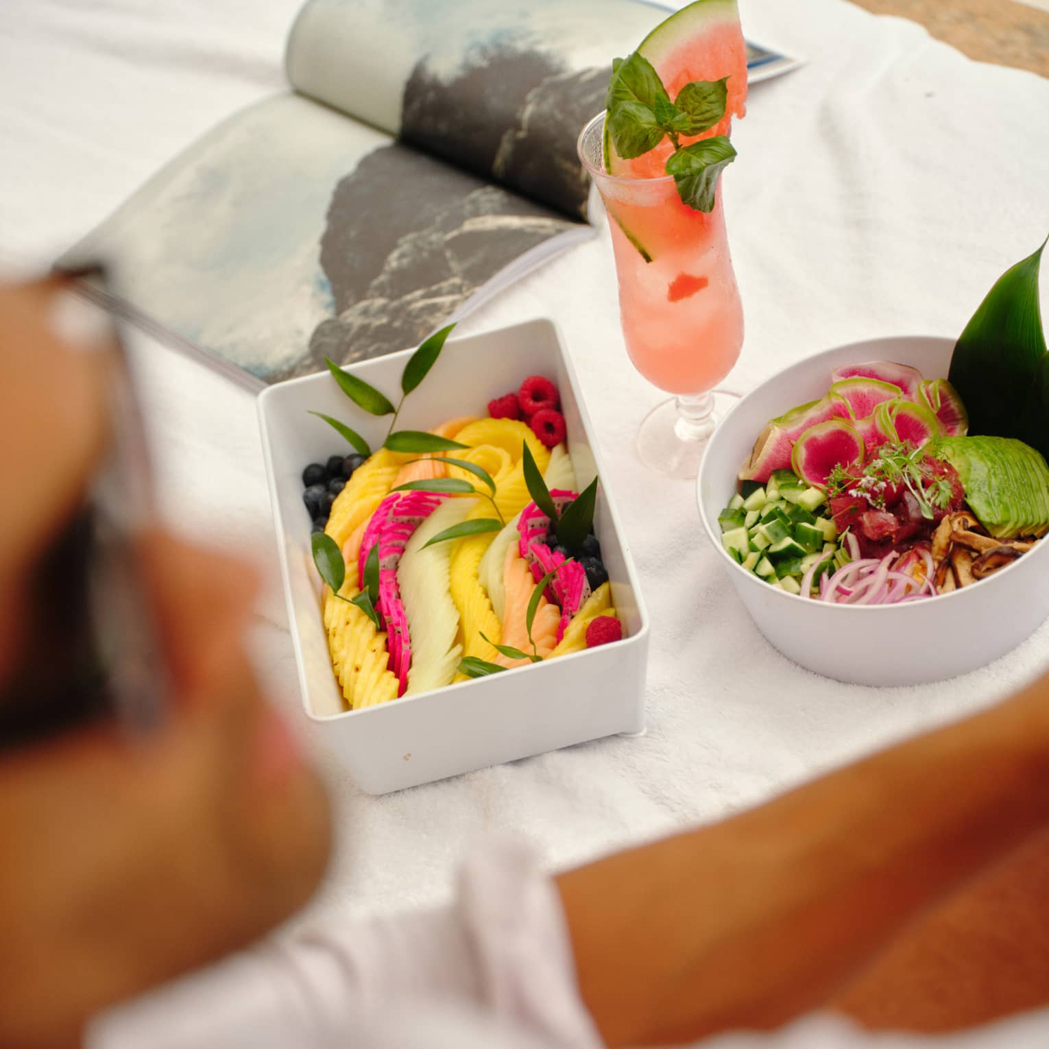Fresh fruit and salad in white containers set on a day bed