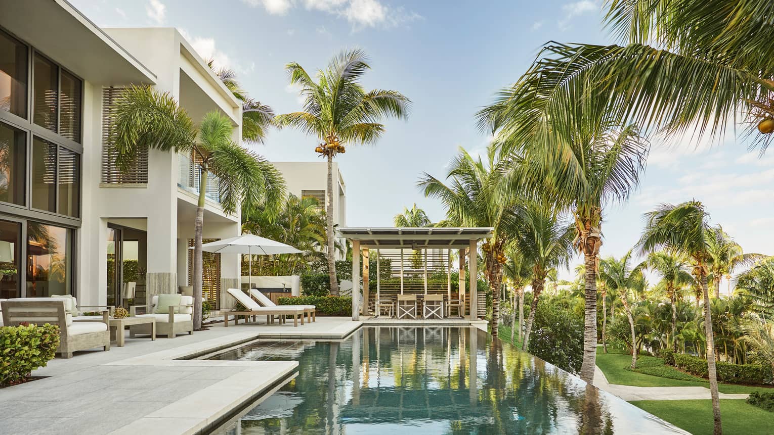 Tall palm trees reflecting on private pool on patio under two storey white villa