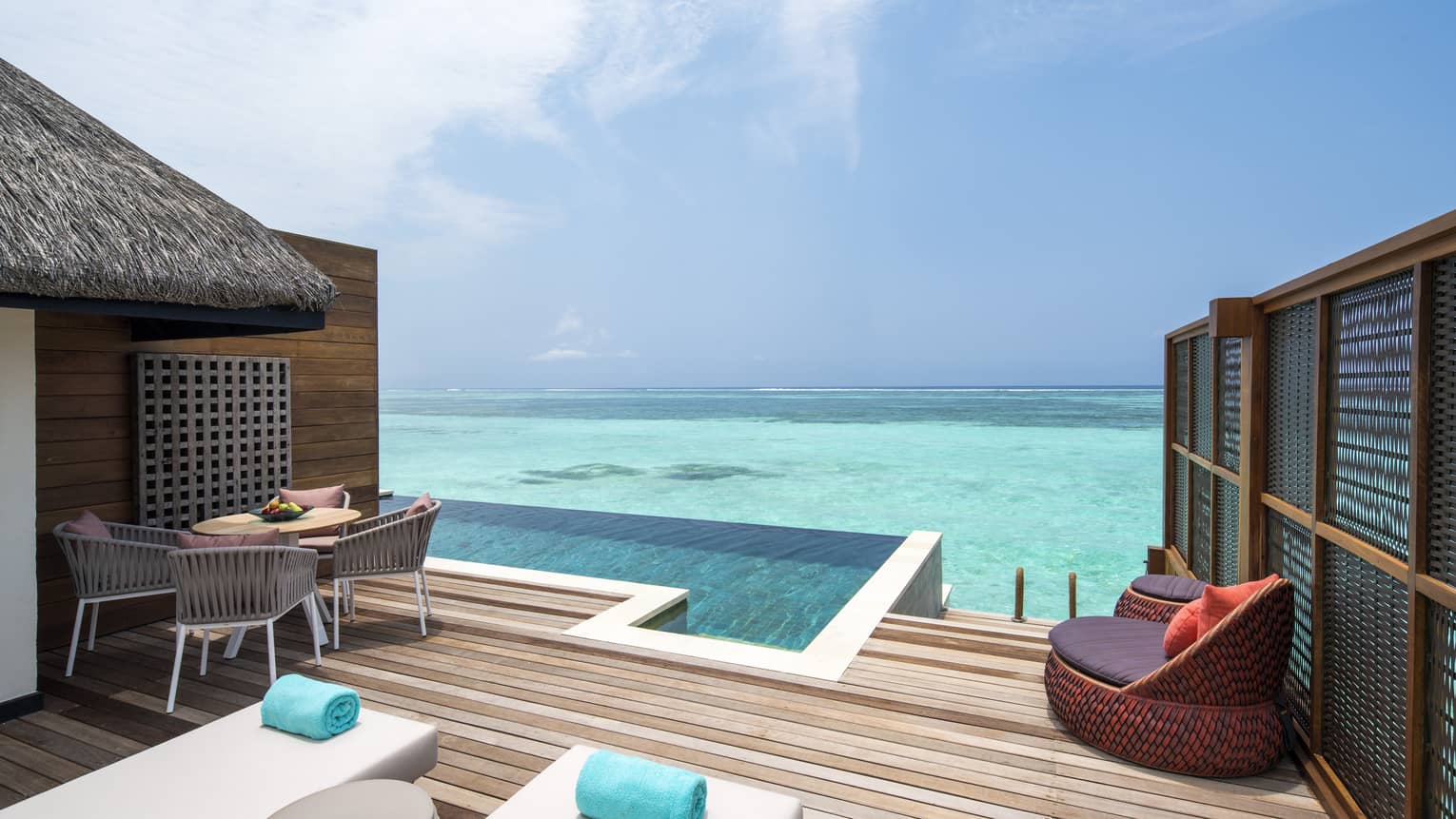 Outdoor lounge area with daybeds, infinity pool, dining setup and a stunning sea view from a family water villa