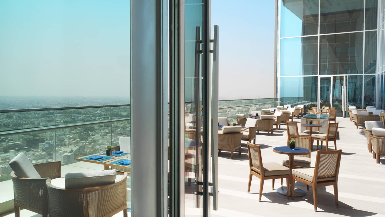 Dining tables and chairs on sunny patio high up on high rise, glass balcony overlooking Kuwait city 
