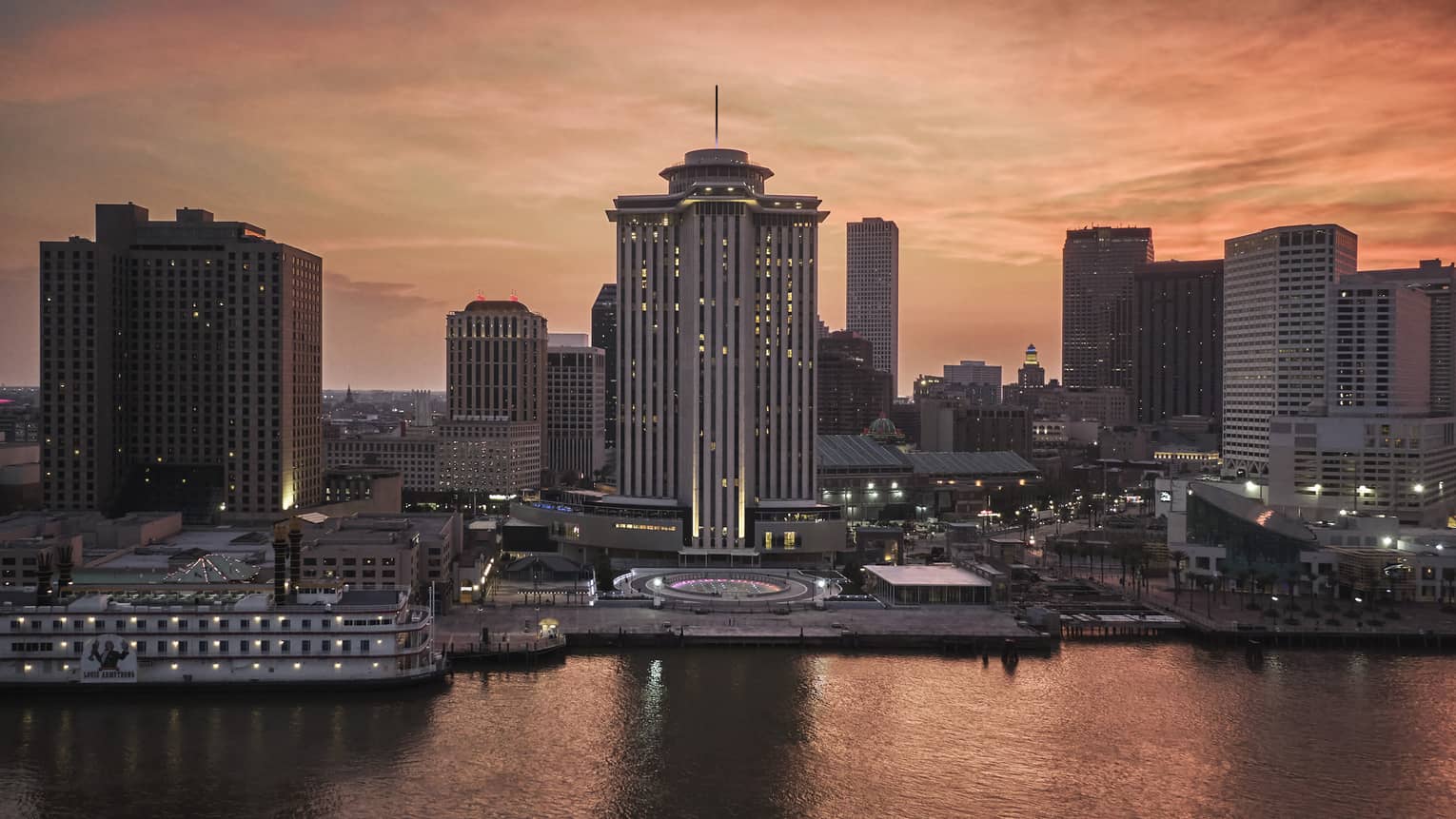 The exterior of a tall building next to a body of water with a city in the background.
