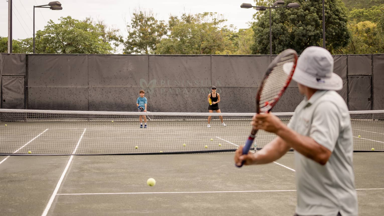 A man, woman and young boy holding racquets on a tennis court