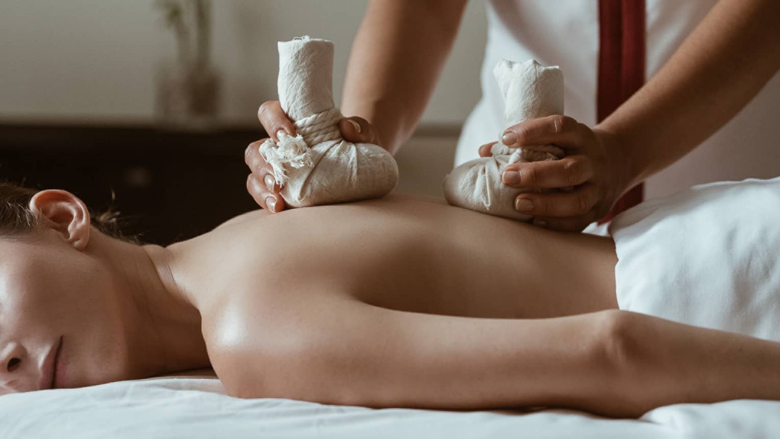 A woman being massaged by heavy stones in cloth bags.