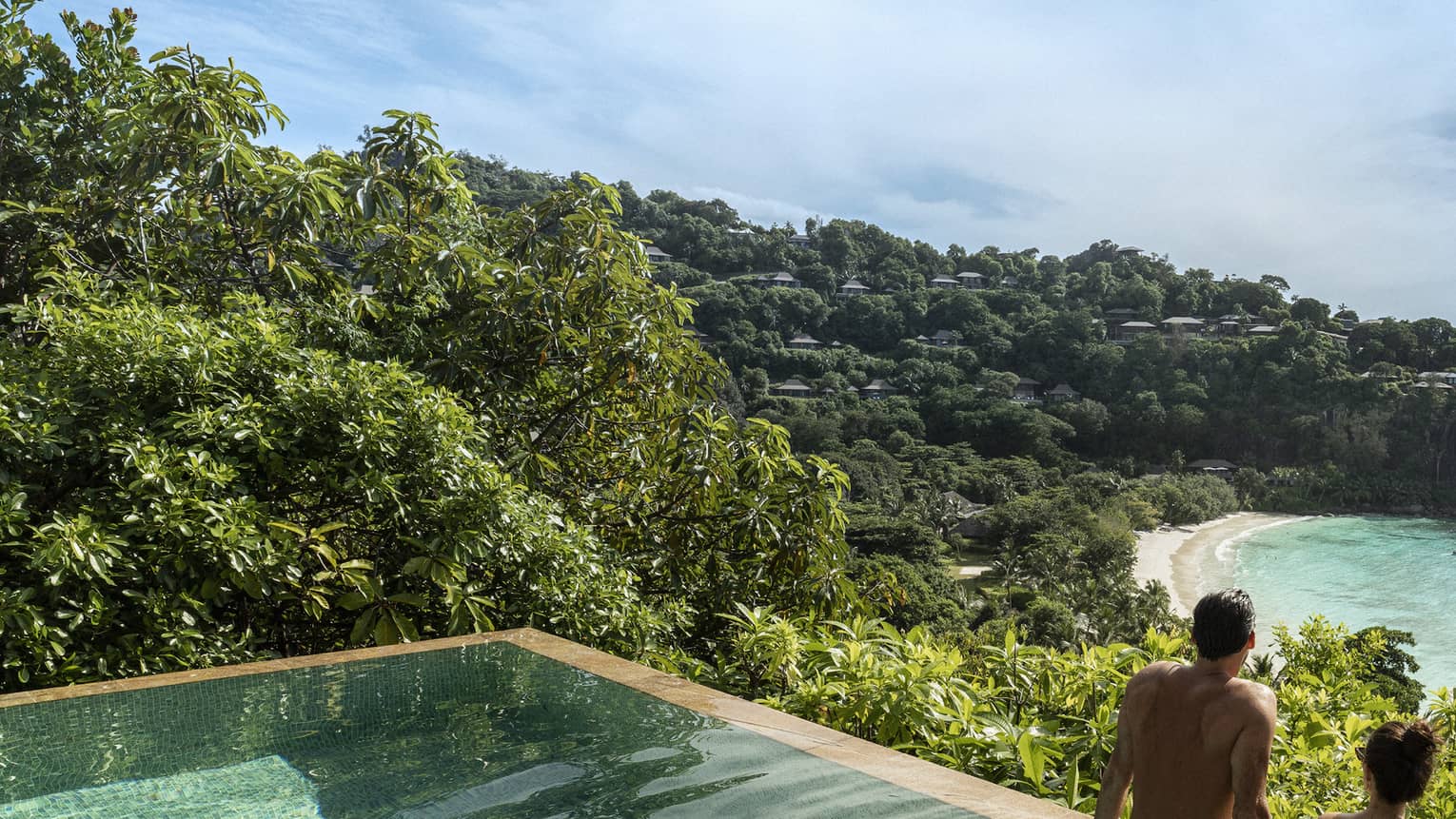 A couple looks out at a view of crystal blue waters and cliffs from an infinity pool