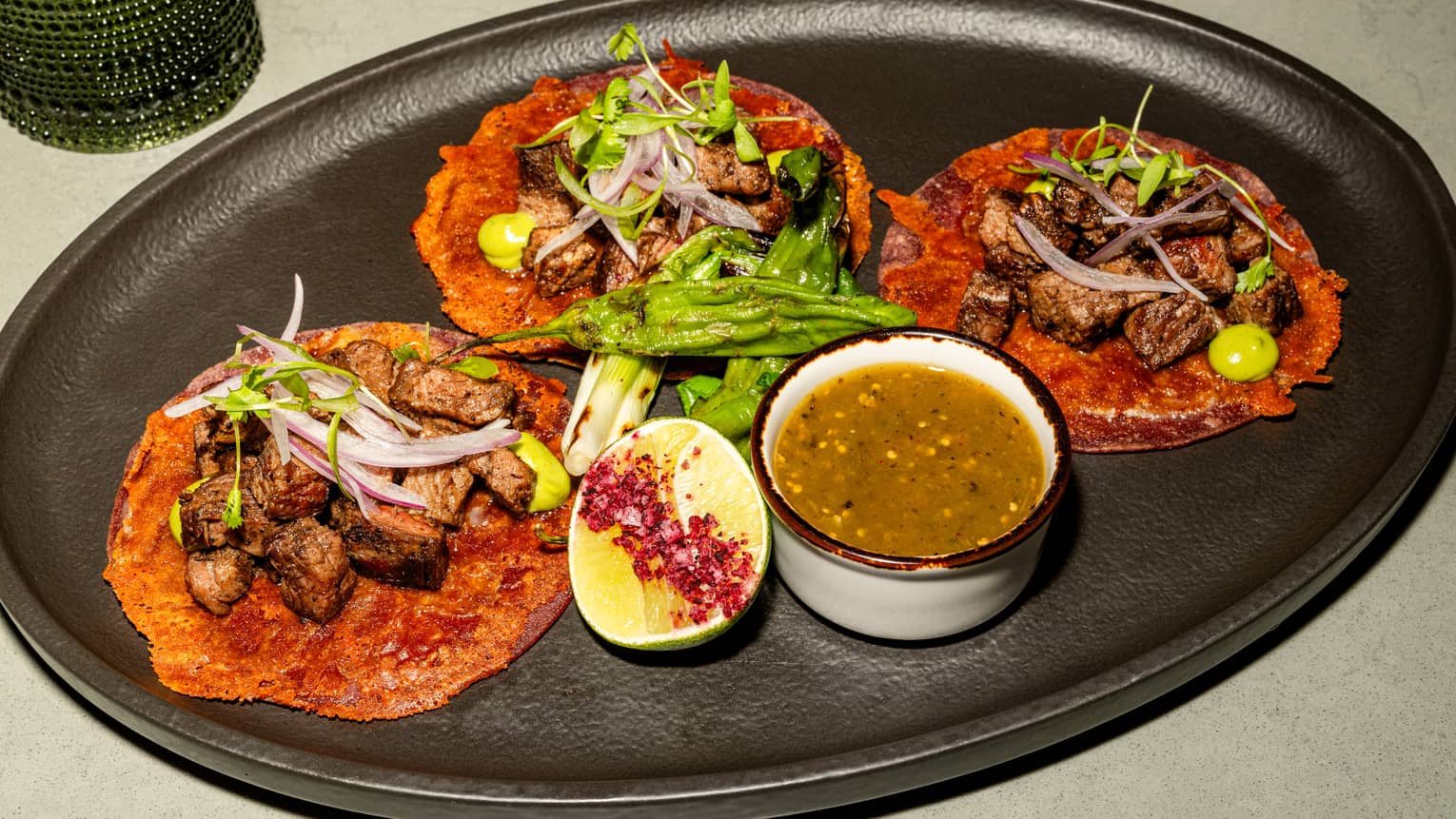 A black oval platter holds colourful food items, garnishes and a small bowl of sauce.