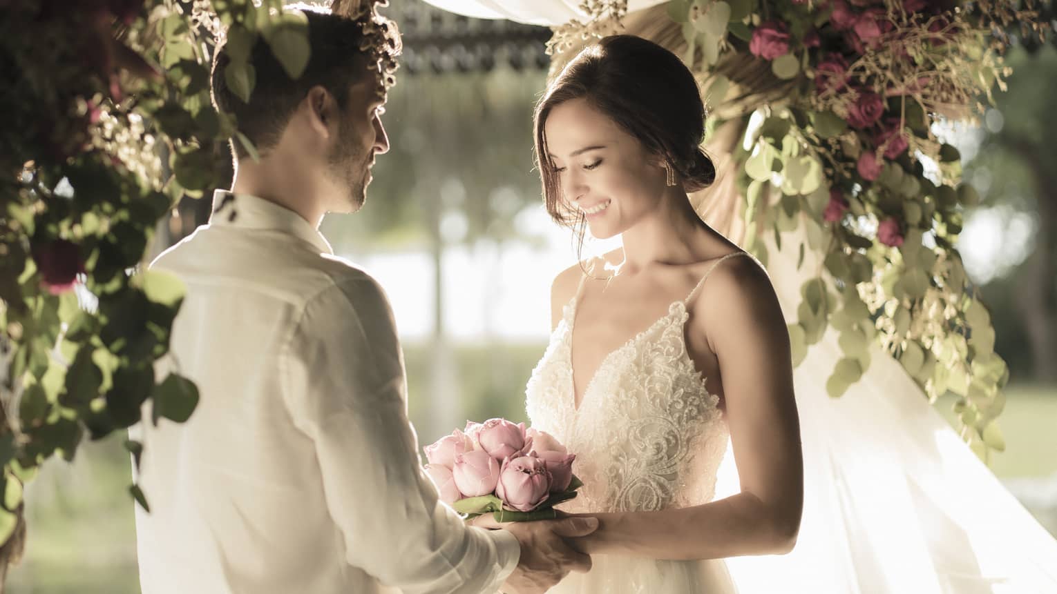 A man and woman are getting married under a pink and green floral arbor with tons of warm natural light