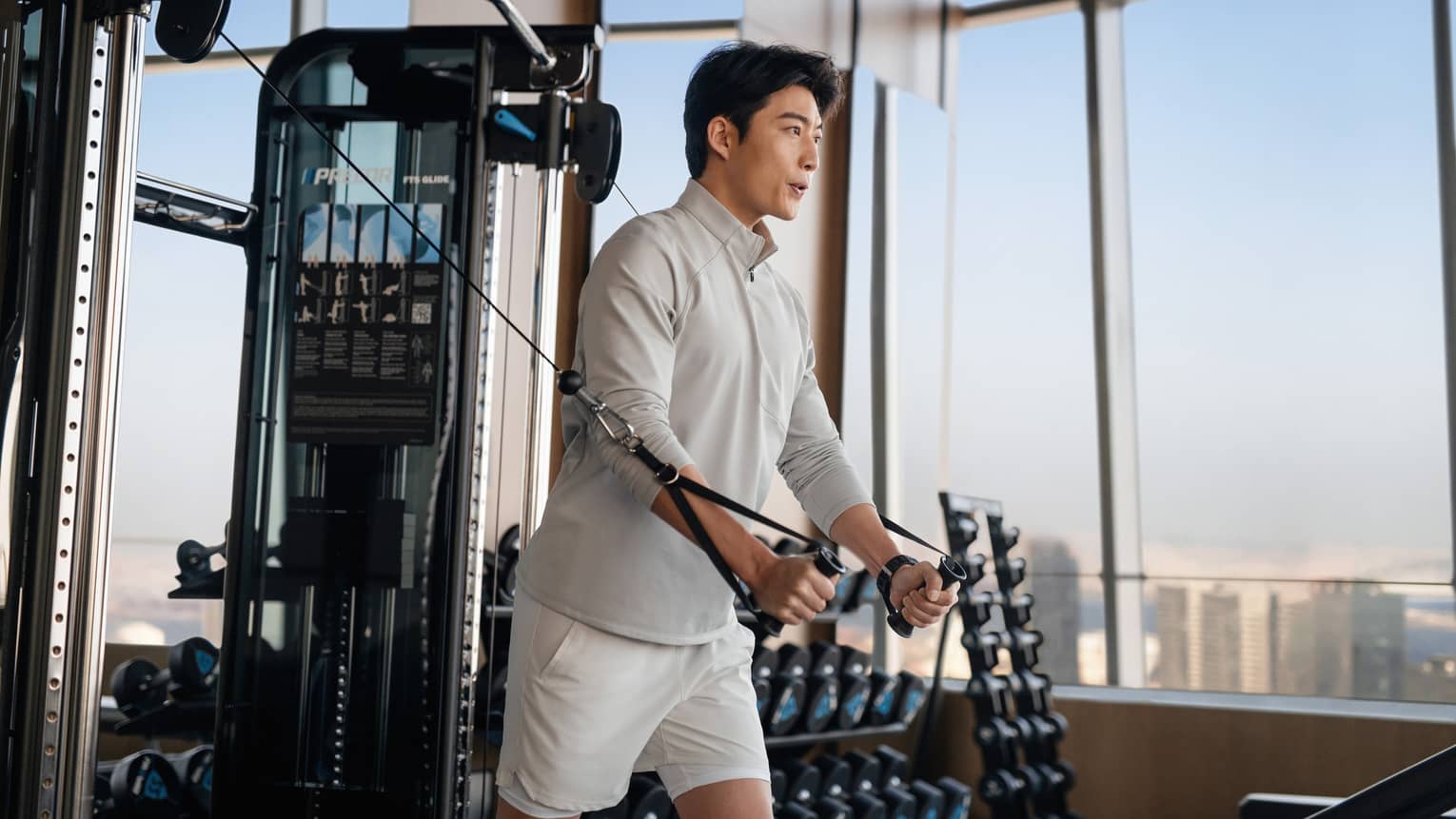 Flanked by large windows overlooking the city and rows of dumbbells, a guest pulls on the weighted levers of a cable machine.