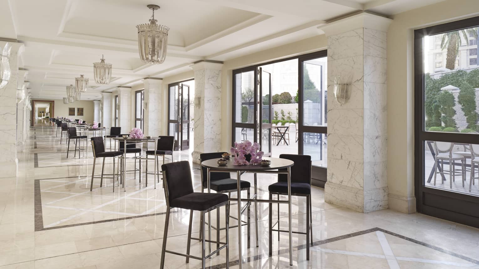A series of black cocktail chairs and tables set up in a marble pre-function area.