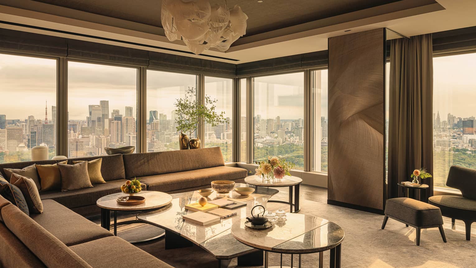 Luxury hotel suite featuring sectional sofa, a cluster of coffee tables, modern lighting fixture and city views