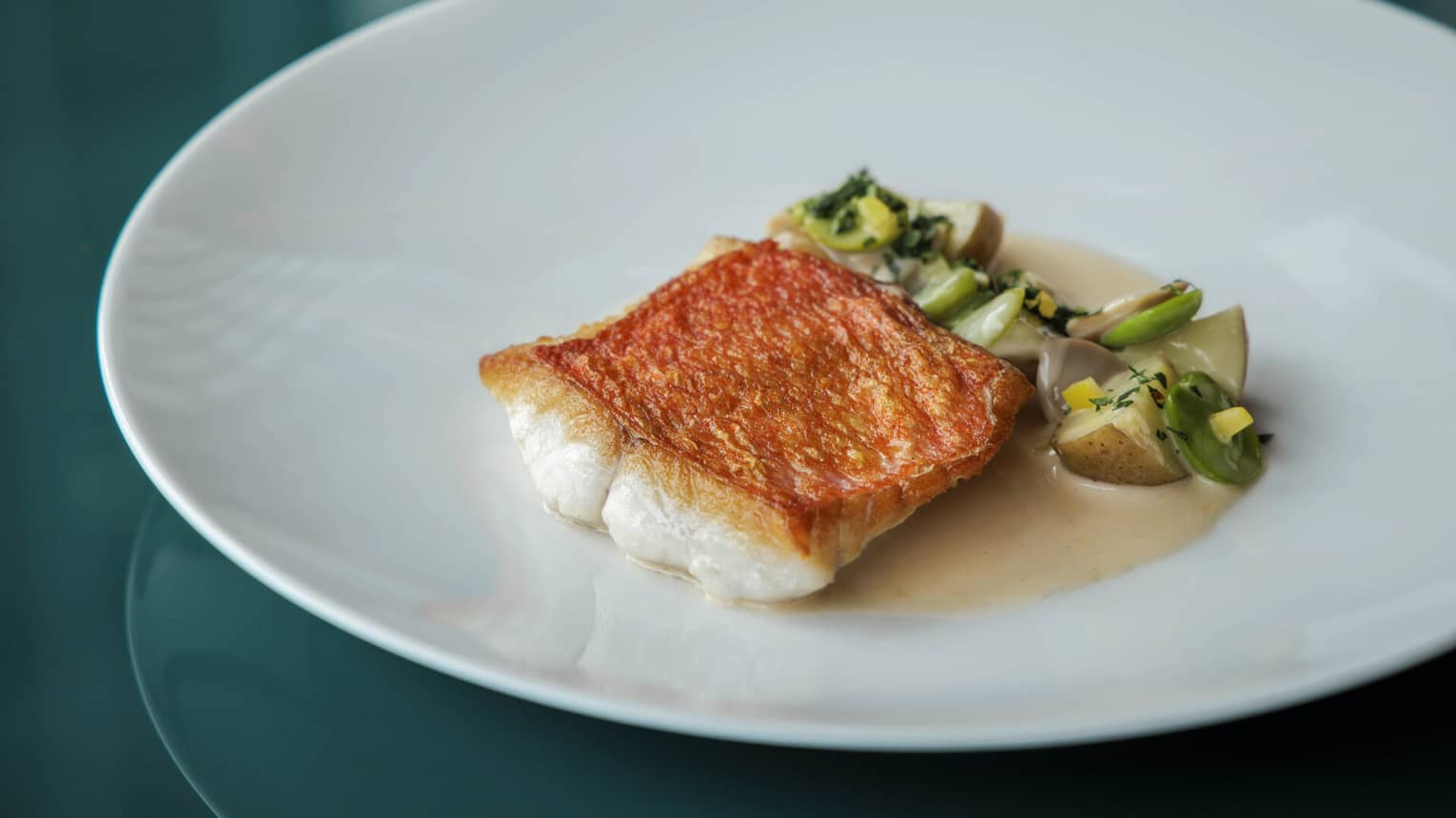 A seared fish served with vegetables on top of a brown sauce