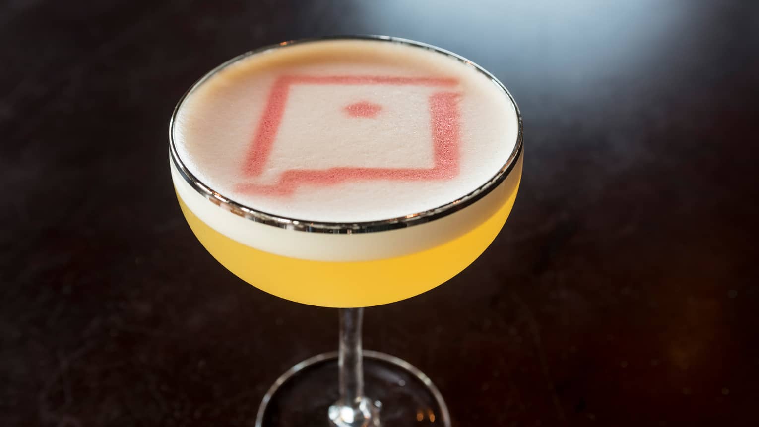 Yellow cocktail in glass topped with foam, red design