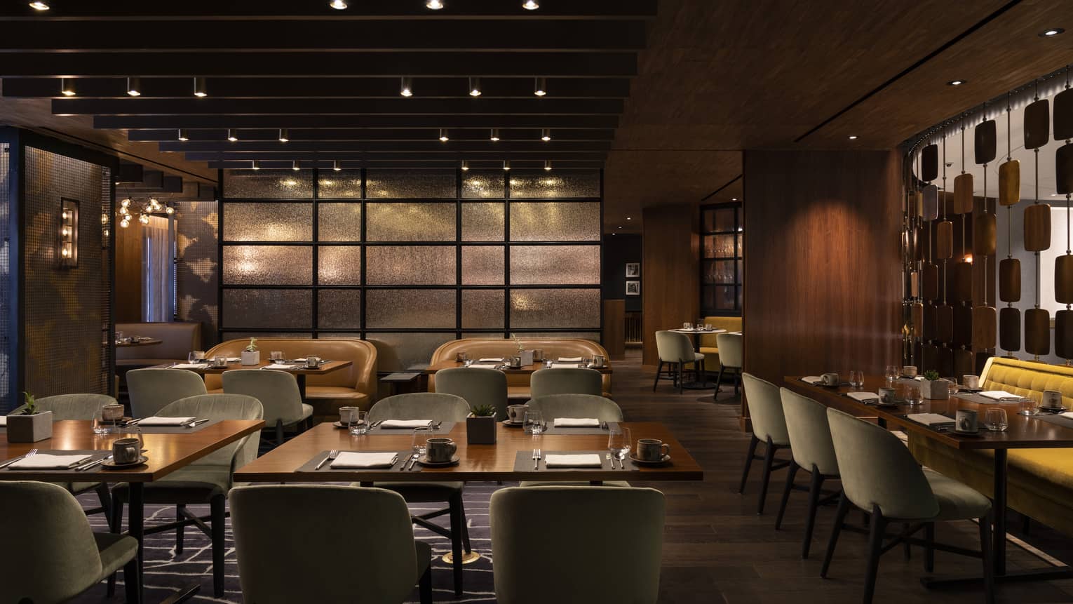 The interior of a dimly lit restaurant with square tables, grey chairs and wood walls.